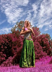 Dancer outdoors in a pink flowery field holds hands to chest with eyes closed.