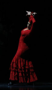 Flamenco dancer in long red dress crosses wrists above head.