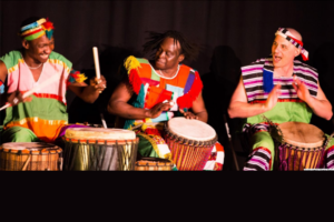 Three seated African drummers in brightly colored clothing.