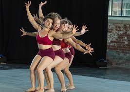 Group of young dancers lined up bending their knees and leaning back on each other as they reach their arms outwards