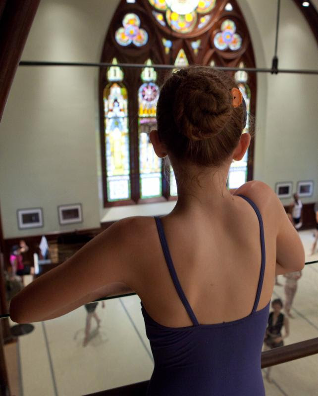 Young ballet dancer in a blue leotard and a bun looks at the Jose Mateo Studio from above.