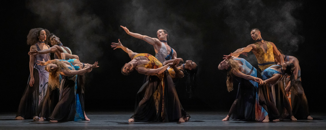 Three groups of dancers in a dim lit stage make elaborate shapes leaning on and away from each other.
