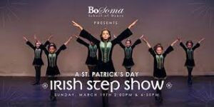Irish step dancers on stage with arms up in a "V" shape.