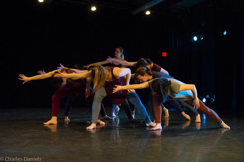 Dancers on a stage clumped together in a deep lung towards stage right.