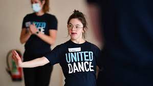 dancer with black United Dance shirt reaches right arm to their side.