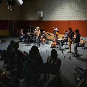 Musicians play their instruments and sing in a performance room with an audience.