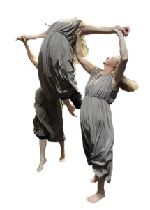 Two dancers in matching grey dresses lift a third dancer by the arms as the latter arches back.