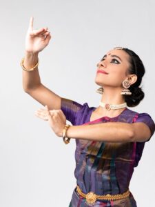 Yamini Kalluri in traditional Kuchipudi attire holds arms bent in front of body on a high diagonal and gazes up above arms.