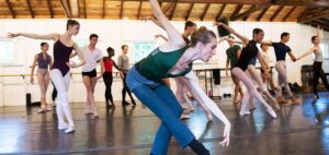 Ballerina Wendy Whelan reaches towards her pointed foot while young dancers behind her follow her example.