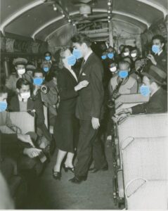 Antique black and white photo with multiple people in social attire with blue surgical masks edited over their noses and mouths.
