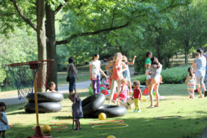 families outdoors in a park setting play with large black donut tires and other game equipment