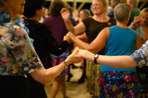 Many people dancing in a room together in pairs holding hands.
