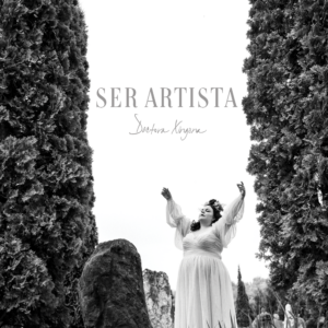 Black and white photo of Doctora Xingona in the center with arms raised in a white dress, outdoors, framed by trees.