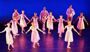 Young dancers in pointe shoes and long tutu's stand in a B+ position.