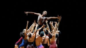 Photo of Complexions dancers clumped together lifting one of the dancers with wide spread arms.