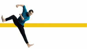 Dancer in black pants and teal long sleeve shirt bends one knee while off balance on opposite heel, arms bent towards bent leg.