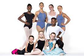 Group of students in different ballet attire ranging in age and race.