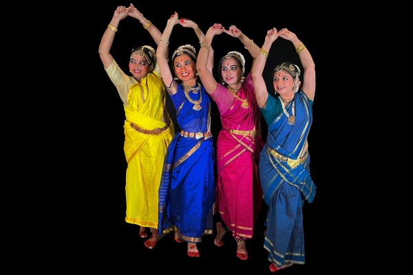 Four dancers in different colored costumes line up on a diagonal with arms up overhead.