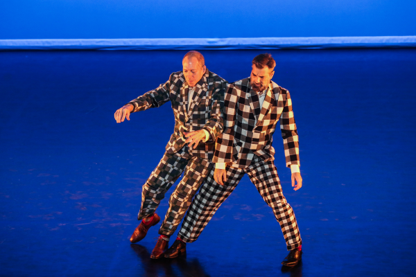 Two dancers in checkered suits lean on each other