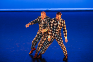 Two dancers in checkered suits lean on each other sideways.