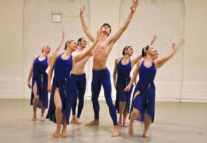 Photo of Alison Cook Beatty Dance Company performing. Dancers in blue costumes reaching arms up.