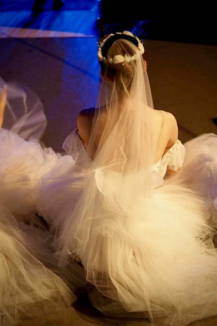 Photo of seated ballet dancer facing away from the camera in white tutu and veil.