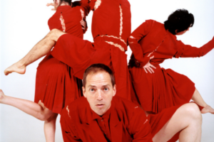 Man in red crawling under twisting bodies dancing in red