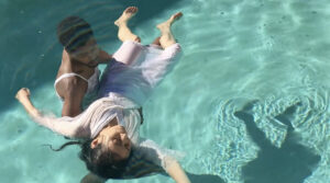 A man holds up a floating woman in a pool.