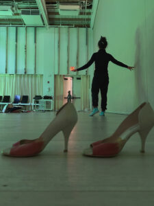 A woman walks away from a pair of empty red and white high heeled shoes.